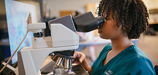 A female student uses high power microscope to examine samples in the lab.